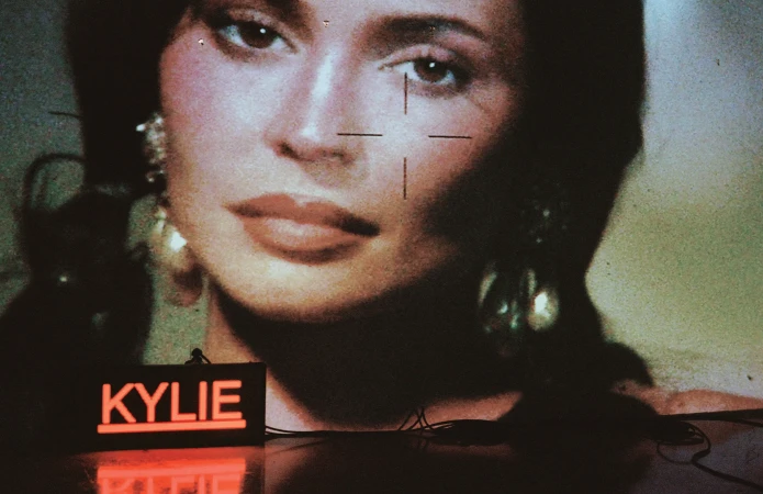 Close-up portrait of Kylie Jenner projected on a textured screen with a glowing neon Kylie sign below.