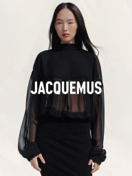 Model wearing a sheer black top and matching skirt against a plain light background with bold white brand typography overlay.