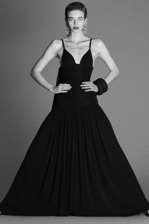 Model wearing a black sleeveless evening gown with a pleated skirt against a plain grey backdrop.