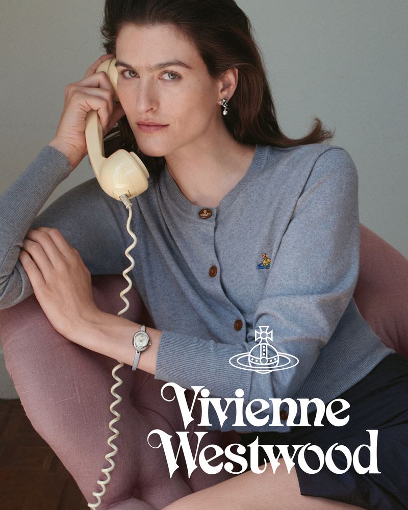 Woman in grey cardigan holding a cream rotary phone handset sitting in a pink armchair