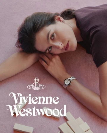 Woman in dark top lying on a textured pink surface next to wooden blocks wearing a metal wristwatch