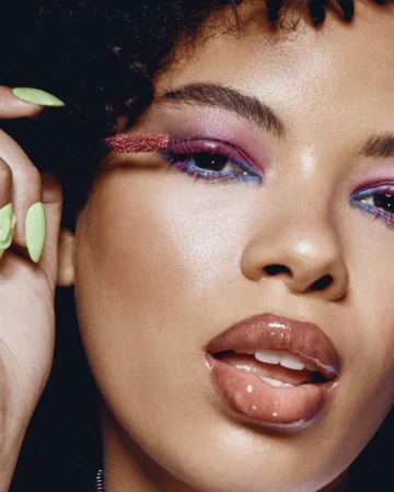 Close-up portrait of a woman applying pink mascara with a wand, featuring vibrant eye makeup and lime green long nails for Kiko Milano Club K