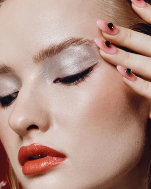 Close-up beauty portrait of a woman with metallic silver eyeshadow, red lipstick, and pink almond-shaped manicured nails.