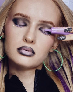 Close-up portrait of a blonde model with dark eye makeup and purple lipstick applying makeup with a tube for KIKO Milano.