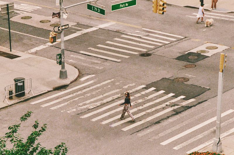 High-angle view of a person walking across a city crosswalk at E 79 St and Park Av.