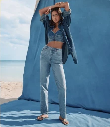 Model in denim outfit standing against a bright blue backdrop on a sandy beach