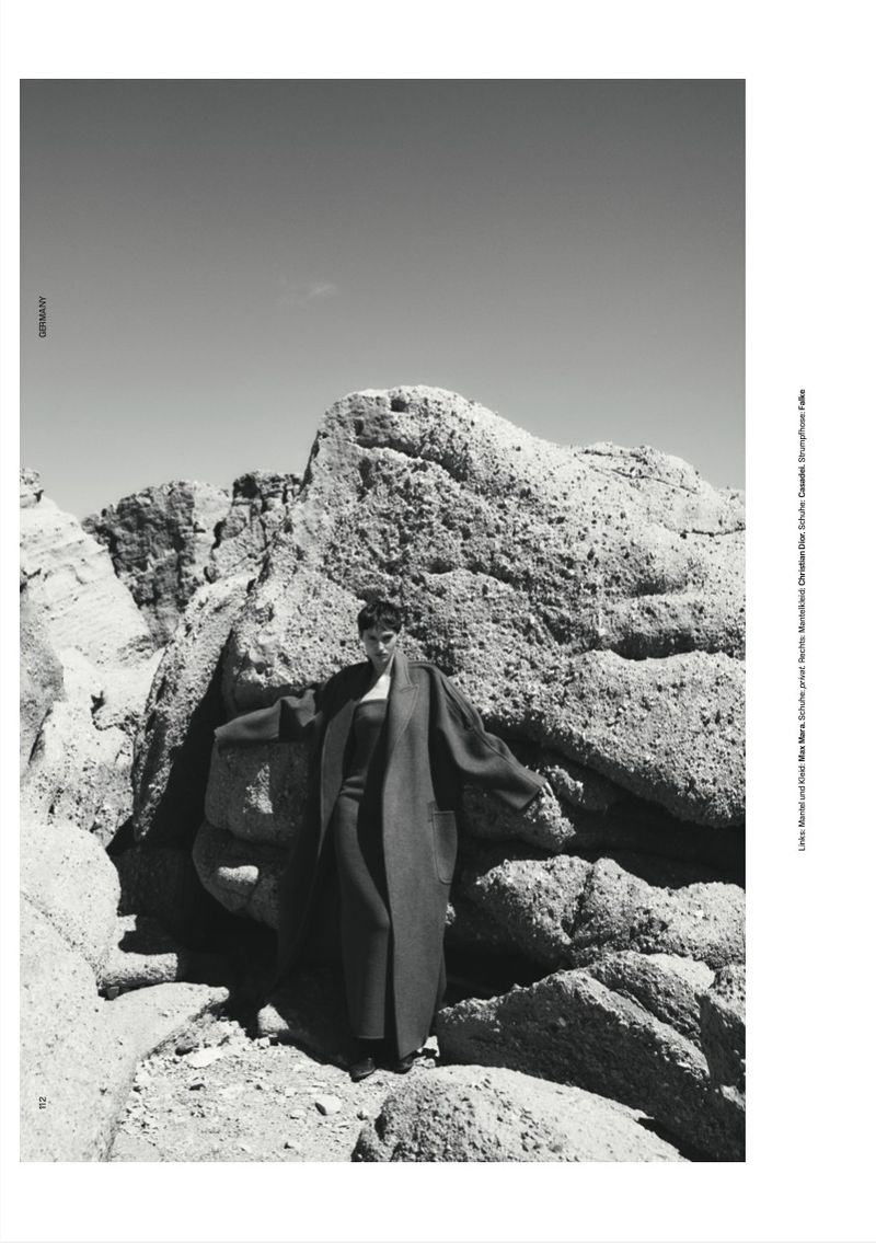 Monochrome fashion editorial featuring a model posing against large rocky boulders outdoors for T Magazine Germany