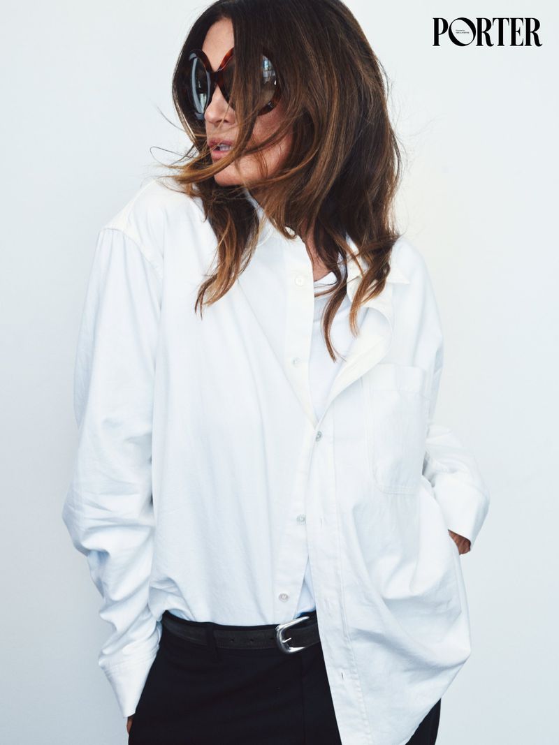 Cindy Crawford wearing oversized sunglasses and a white button-down shirt against a clean white backdrop