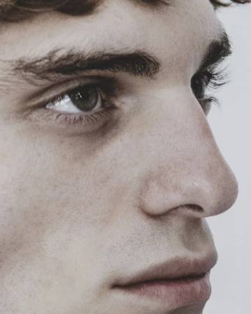 Extreme close up profile portrait of a young man with freckles and natural skin texture against a plain light background