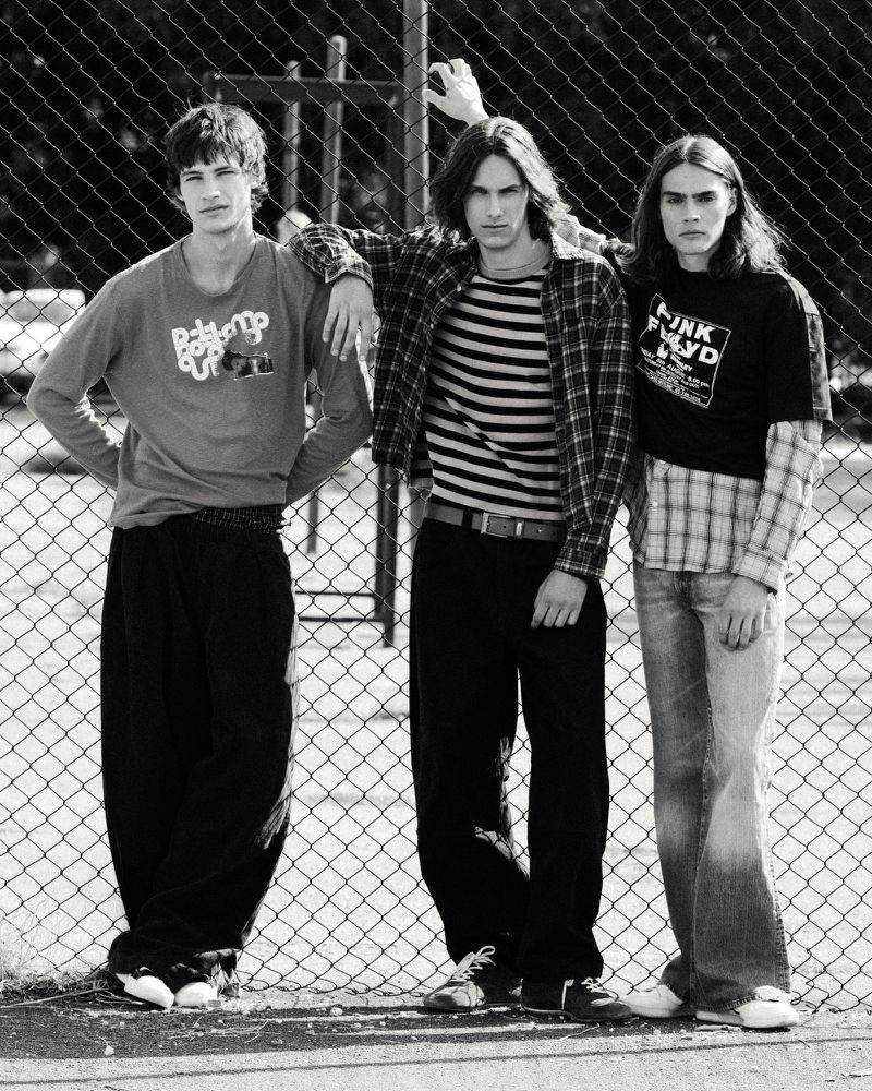 Black and white portrait of three male models posing against a chain-link fence for an editorial project.