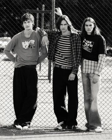 Black and white portrait of three male models posing against a chain-link fence for an editorial project.