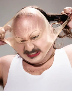 Close-up of a person stretching a nude pantyhose tight over their face and head, wearing a white tank top