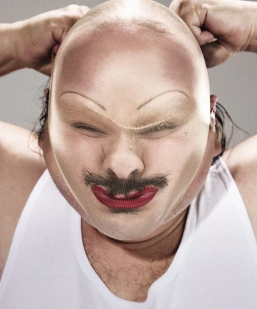 Close-up portrait of a person pulling a nude nylon stocking tight over their face with painted eyebrows, mustache, and red lips