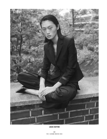 Model Yilan Hua sitting cross-legged on a brick wall wearing a dark blazer and trousers for 10 Magazine Day Shift