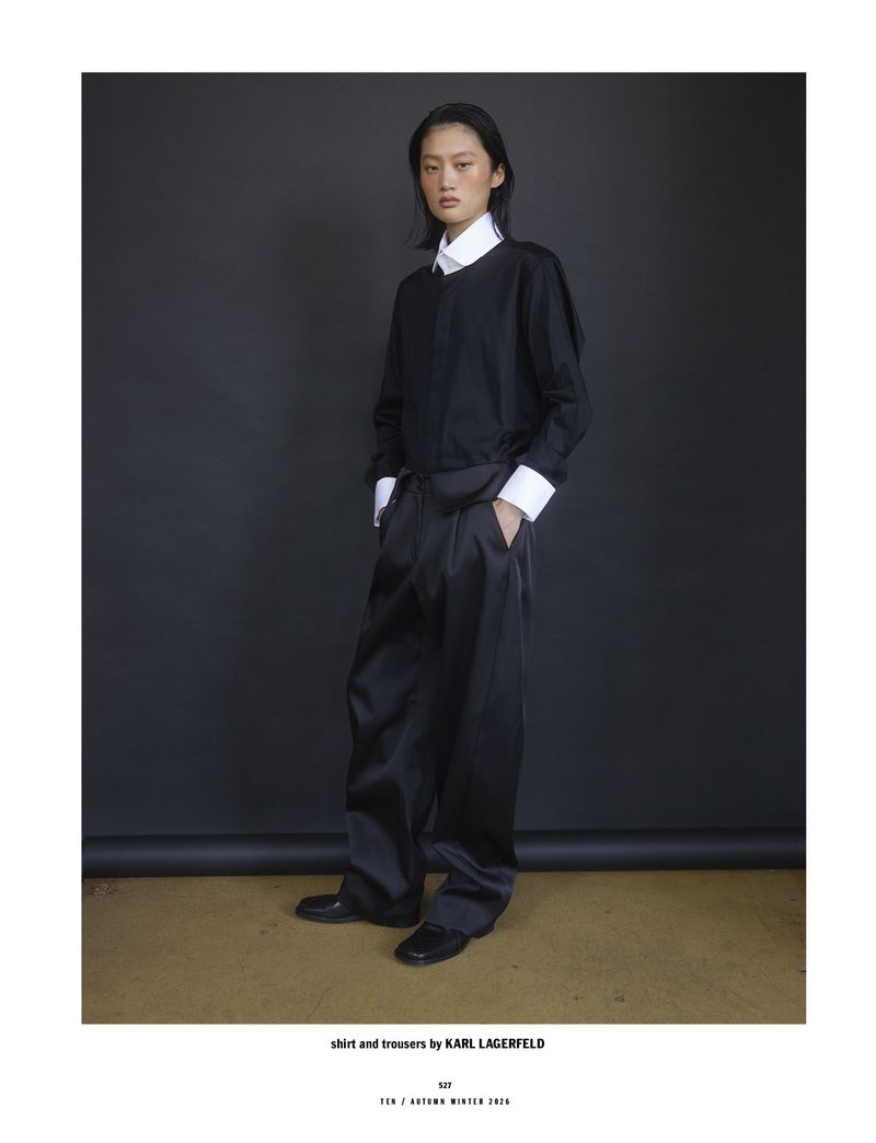 Model in black top and trousers with white shirt collar and cuffs posing against a dark background for 10 Magazine Day Shift