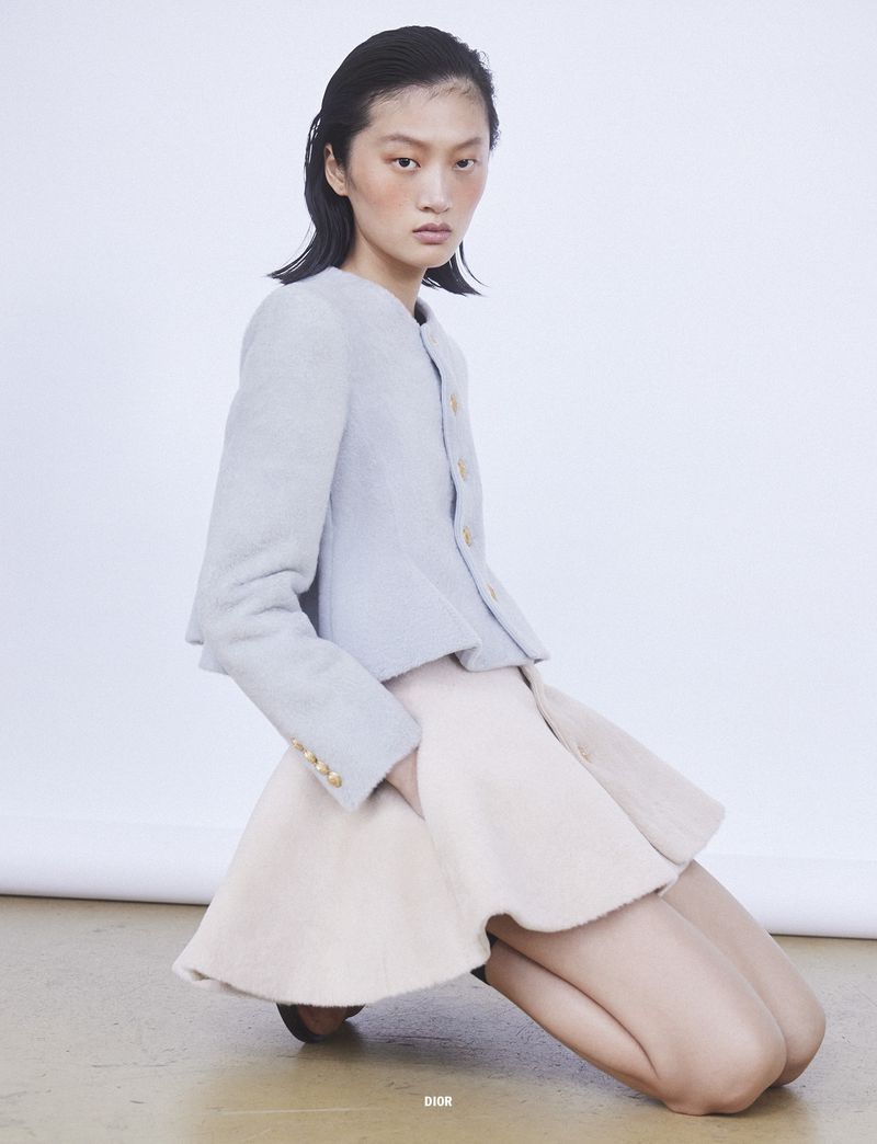 Model Yilan Hua kneeling in a light grey jacket and flared skirt for 10 Magazine editorial Day Shift by Mark Pillai