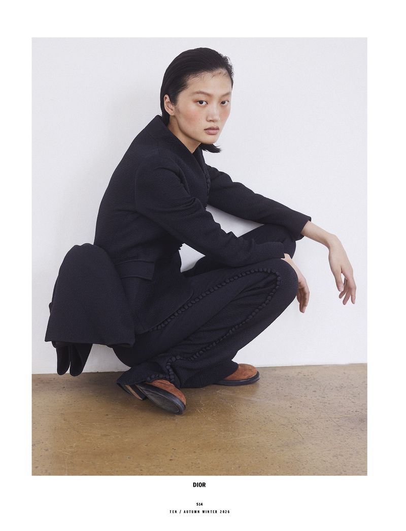 Model Yilan Hua crouching in a black suit against a plain white studio background for 10 Magazine Day Shift editorial.