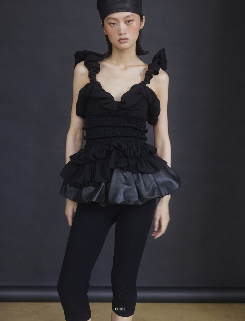 Model Yilan Hua wearing a black ruffled top and matching head covering against a dark studio backdrop for 10 Magazine