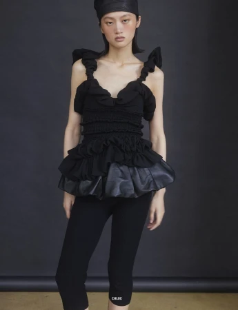 Model Yilan Hua wearing a black ruffled top and matching head covering against a dark studio backdrop for 10 Magazine