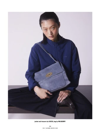 Model Yilan Hua wearing a blue jacket and holding a crossbody bag against a simple studio backdrop.