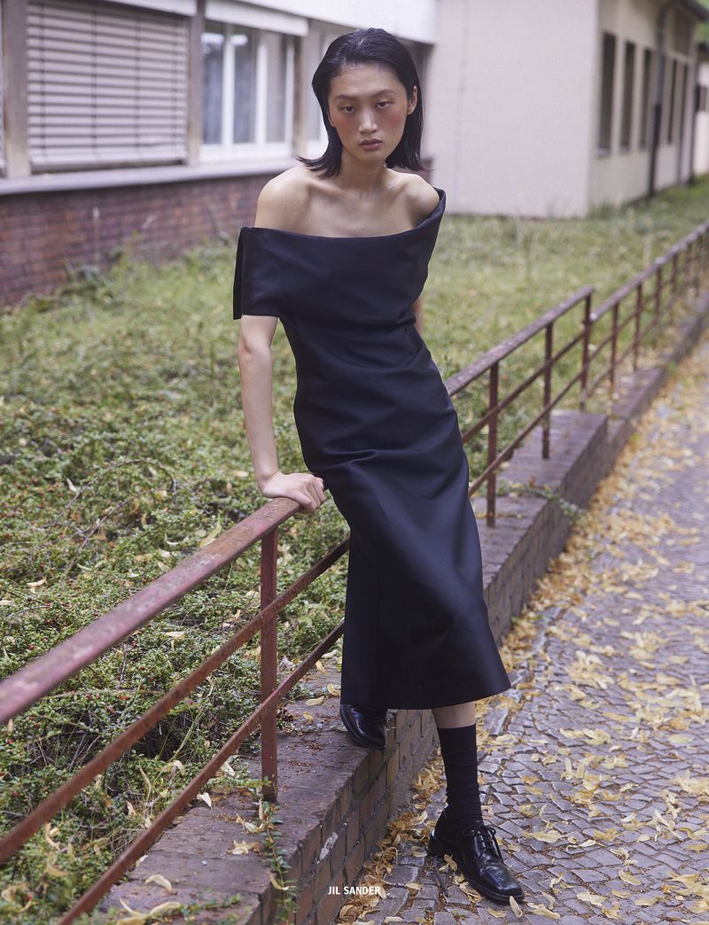 Model Yilan Hua in a black off-shoulder dress leaning against a metal railing outdoors for 10 Magazine Day Shift editorial