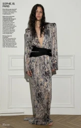 Model in a metallic printed gown with a black sash standing against white wall molding