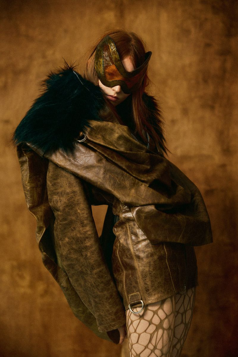 Model wearing a distressed brown leather jacket with dark fur collar and mask in Elle Hungary's Golden Age editorial