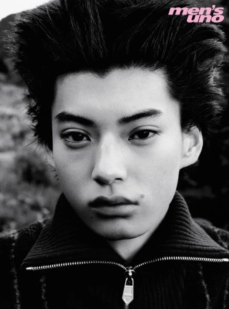 Close-up black and white portrait of a young male model with voluminous spiky hair wearing a zipped turtleneck top.