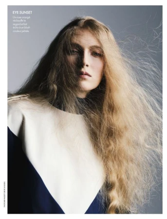 Model with long tousled blonde hair wearing a color-blocked top against a neutral grey studio background