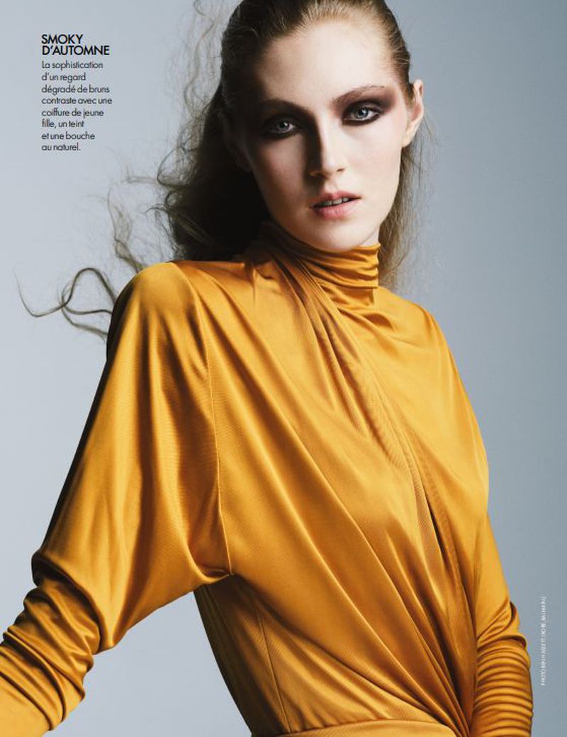 Model wearing a gold satin turtleneck top with smokey eye makeup against a grey studio background for Elle France.