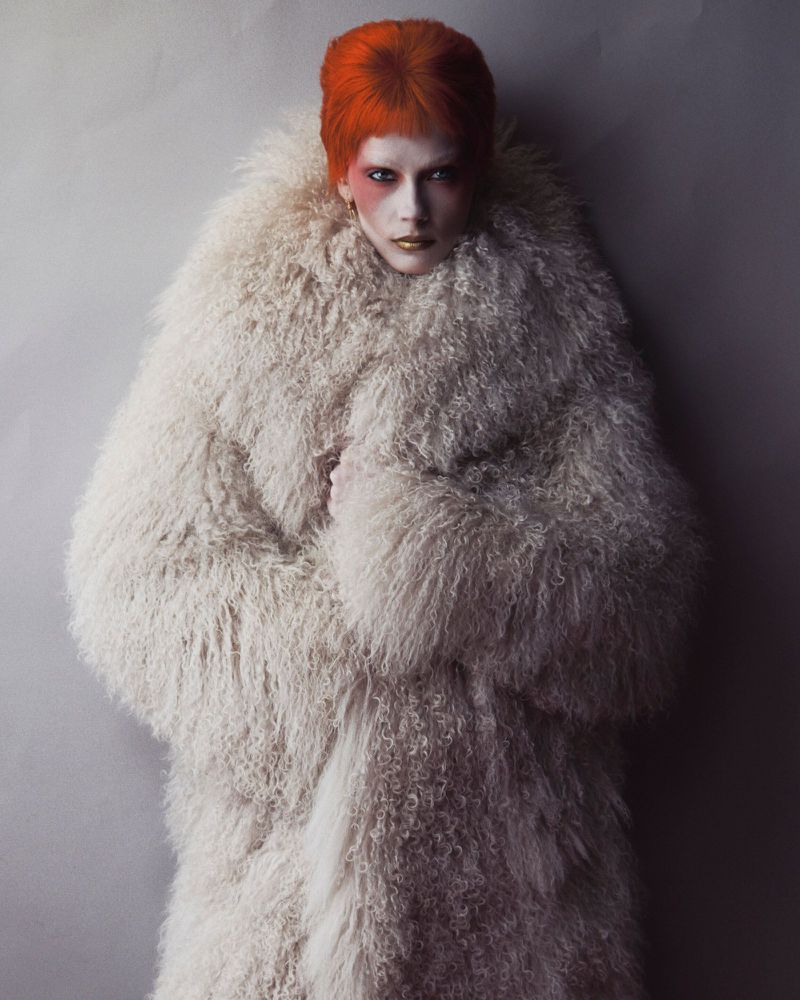 Model with vibrant orange hair wearing a large fluffy white coat against a grey studio backdrop for V Magazine.