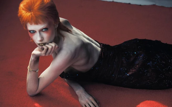 Model with orange hair and dark dress lying on a red carpet surface for V Magazine editorial