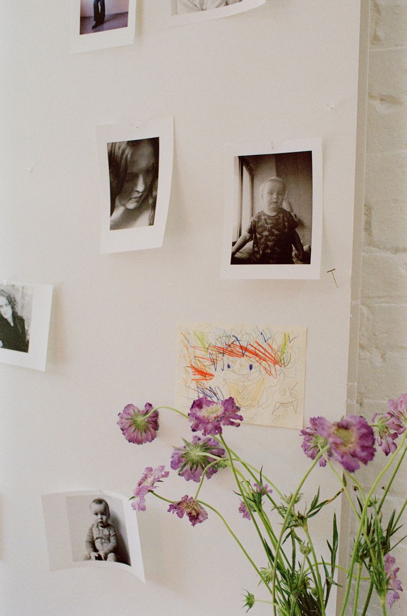 Polaroids and drawings pinned to a white wall behind purple wildflowers