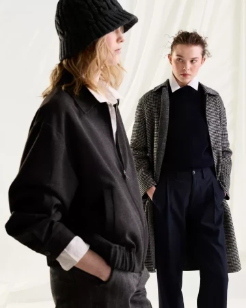 Two female models showcasing winter fashion with a black knit hat, dark jacket, and houndstooth coat against a soft white backdrop.
