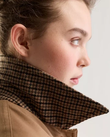 Close-up profile of a model wearing a brown houndstooth collared coat against a plain white studio background.