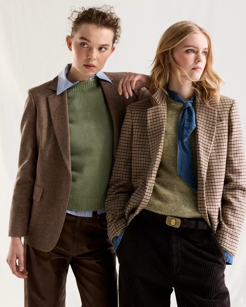 Two female models wearing tailored blazers and knit sweaters against a plain white studio backdrop.