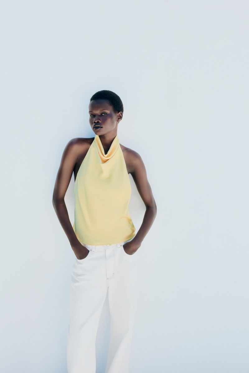 Model wearing a pale yellow halter top and white trousers posing against a bright white background for Zara.