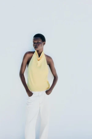 Model wearing a pale yellow halter top and white trousers posing against a bright white background for Zara.