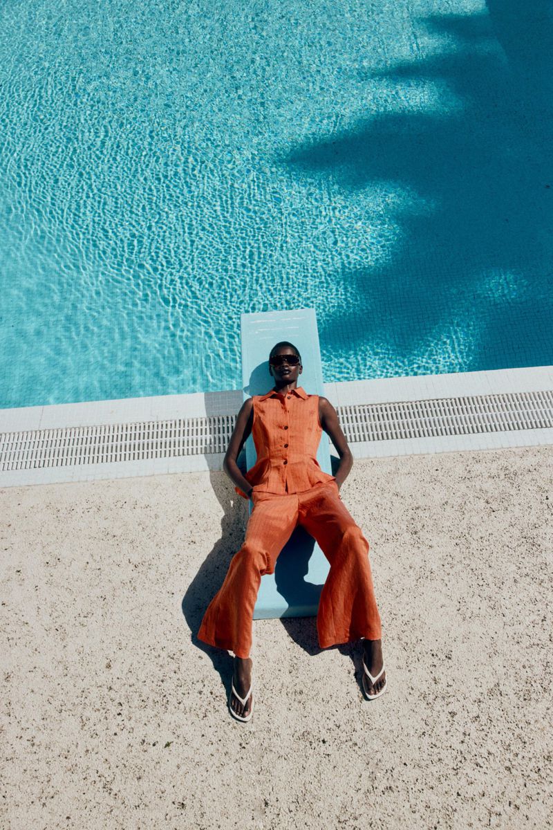 Model in orange sleeveless top and matching trousers lying on a blue diving board by a swimming pool for Zara.