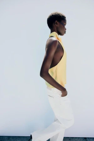 Model wearing a yellow halter top and white trousers against a bright white background