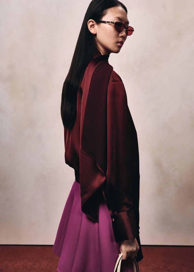 Model in dark red satin blouse and pink skirt wearing sunglasses against a textured background