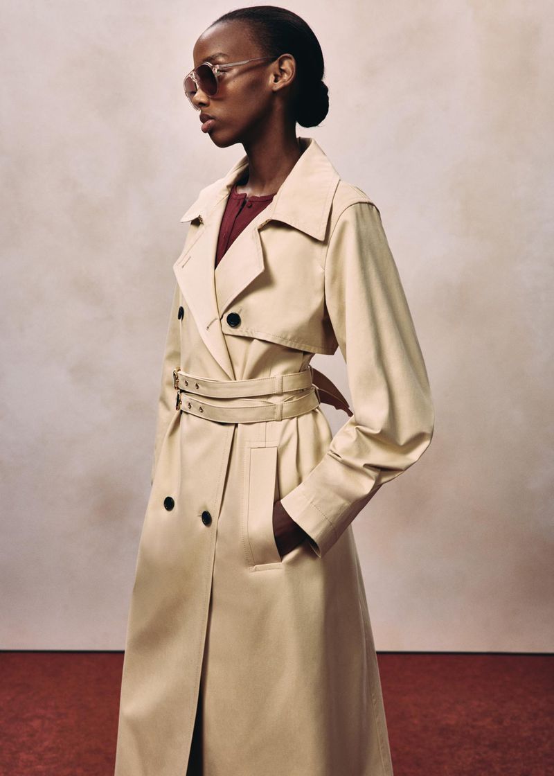 Model wearing a tan belted trench coat and sunglasses against a textured background for HUGO RED FALL 2026.