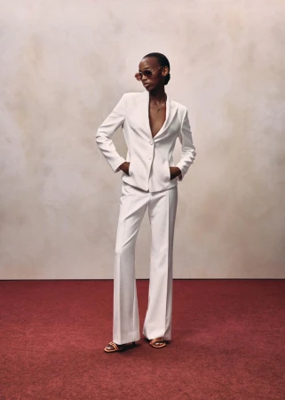 Model wearing a white suit and tinted sunglasses standing on a red carpet against a textured neutral backdrop for HUGO.