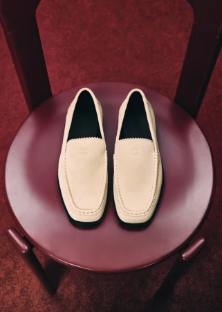 A pair of cream suede loafers resting on a round burgundy wooden chair