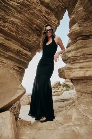 Model Jenn Du Puy in a long black dress standing between dramatic rock formations under an open sky