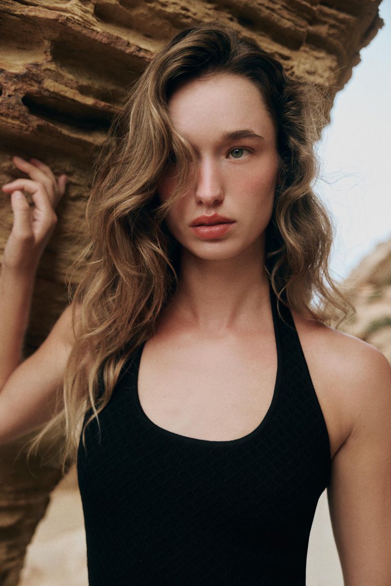 Model Jenn du Puy in a black halter top posing against weathered rock formations outdoors.