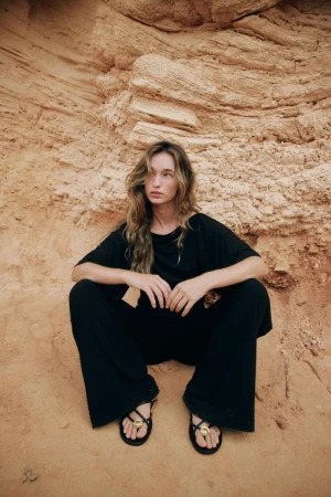 Model Jenn Du Puy in a black outfit squatting against a textured sandy rock formation.