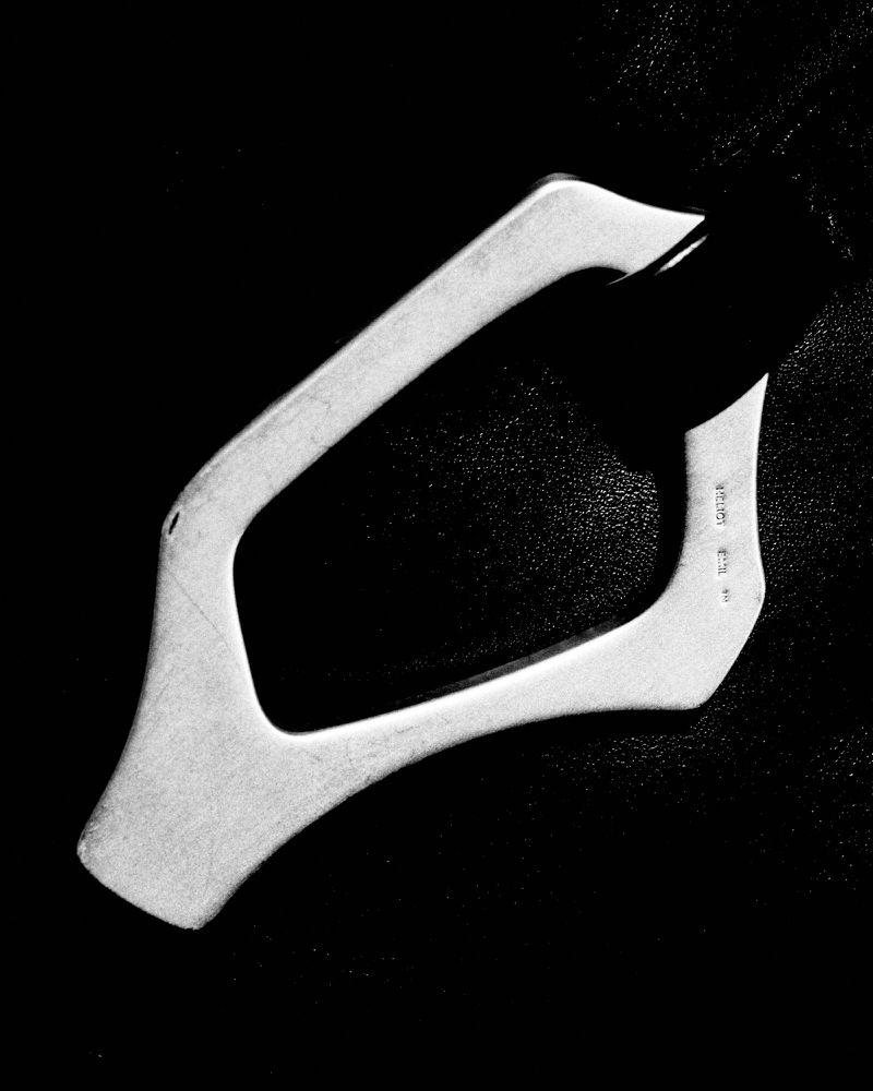Close-up of a metallic bottle opener set against a dark background with subtle surface textures, captured in black and white.