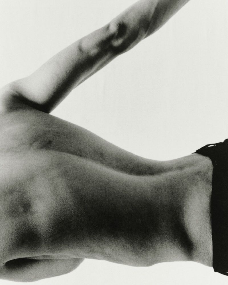 Monochrome image of a man's torso and arm against a bright background, showing muscular definition and form.