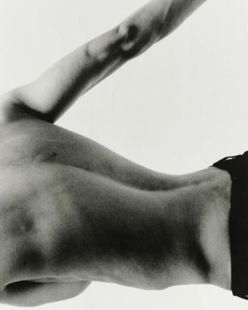 Monochrome image of a man's torso and arm against a bright background, showing muscular definition and form.